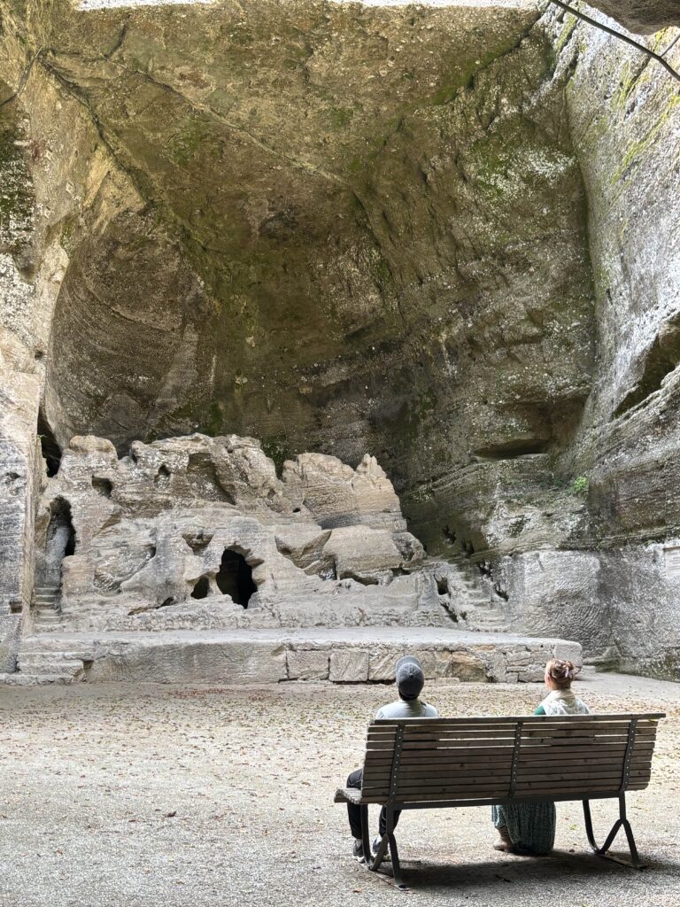 Two people sitting at a bench looking towards a 16th Century Stone Theatre in Hellbrunn Park