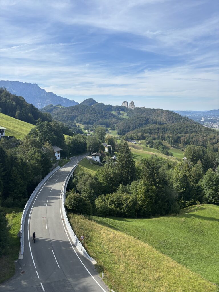 Birds Eye view down to Hallein from the Salt Mine observation deck. It is a bright, sunny day. A road bisects the valley and is quiet except for one cyclist. The Grober Barmstein rocky pinnacles can be seen in the distance.