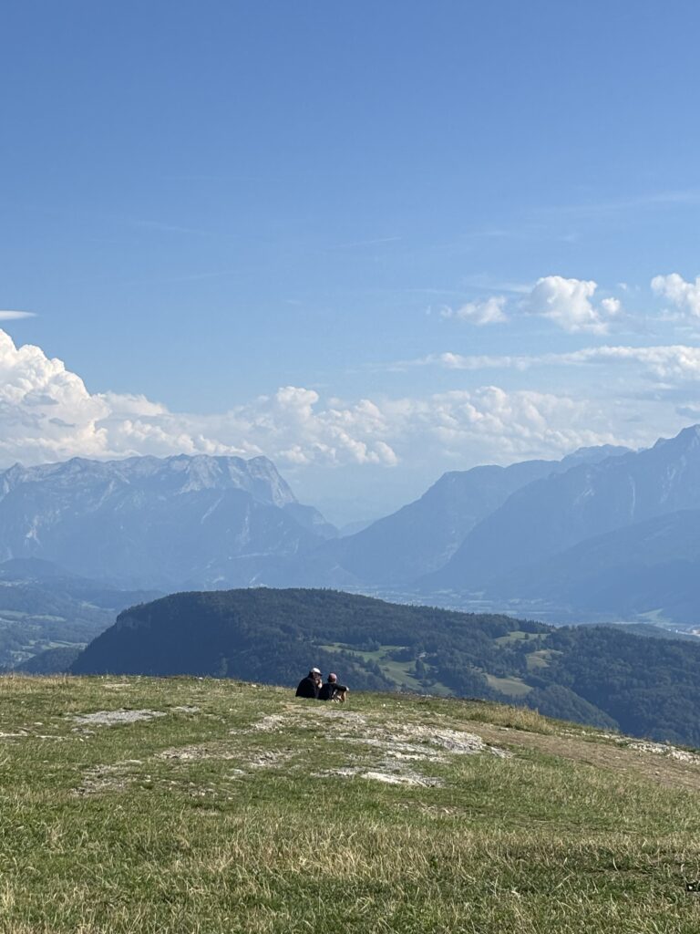 Two people sitting and taking in the panoramic mountain views from Gaisberg Peak overlooking the neighbouring Untersberg Mountain range and surroundings area of Salzburg.